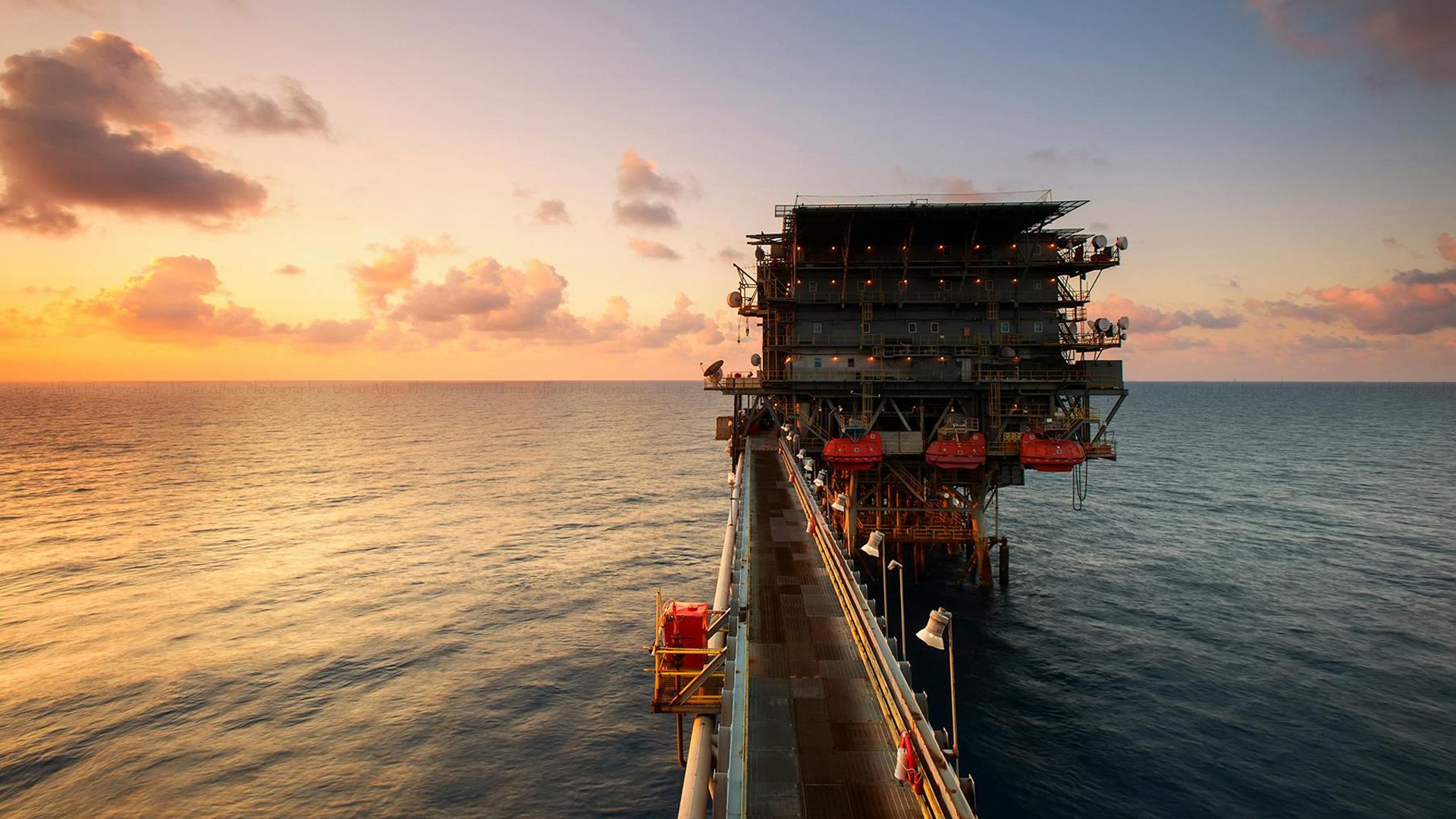 Photo of an oil rig in the sea against a sunset