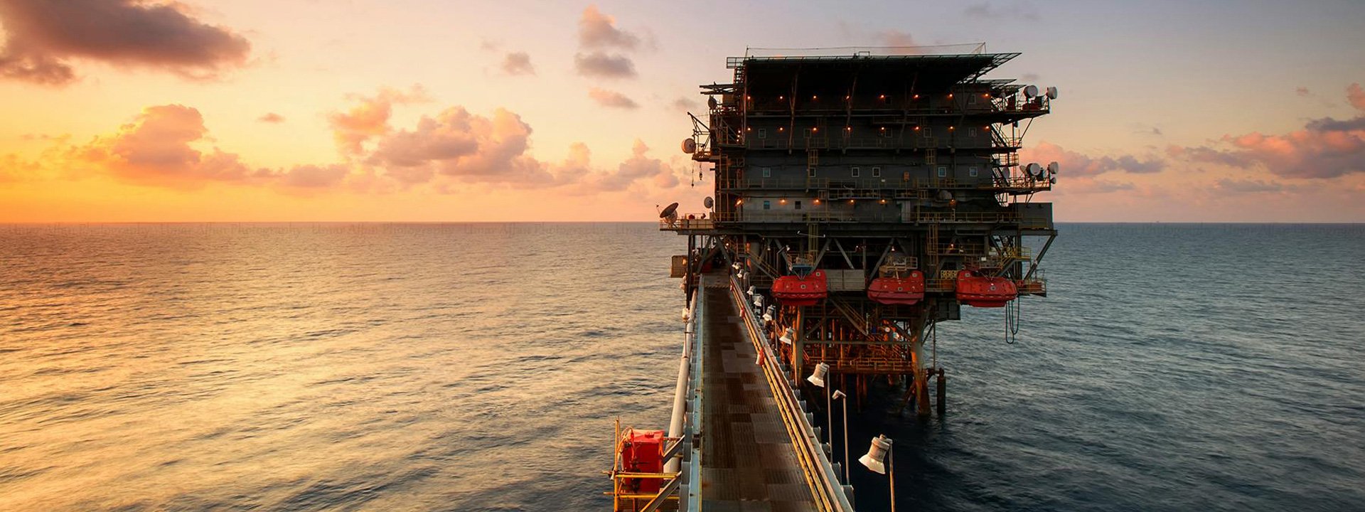 Photo of an oil rig in the sea against a sunset